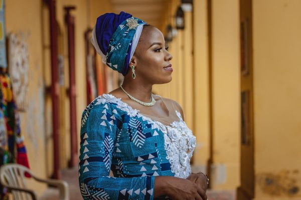 Afro Caribbean woman in a blue dress, she has a head scarf and is smiling